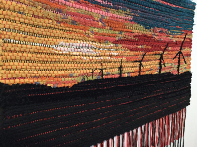 Woven rag wall hanging by fiber artist Petra Guenthner Johnson. Artwork depicts black windmills and foreground silhouetted by a vibrantly colored sunset. 34x22"