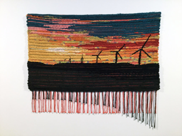 Woven rag wall hanging by fiber artist Petra Guenthner Johnson. Artwork depicts black windmills and foreground silhouetted by a vibrantly colored sunset. 34x22"