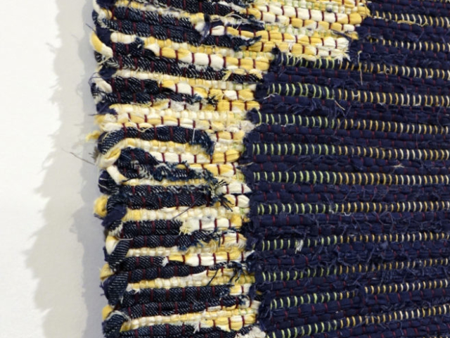 Woven rag wall hanging by fiber artist Petra Guenthner Johnson. Picture shows left selvage detail of solar eclipse in navy denim with white and yellow outline.