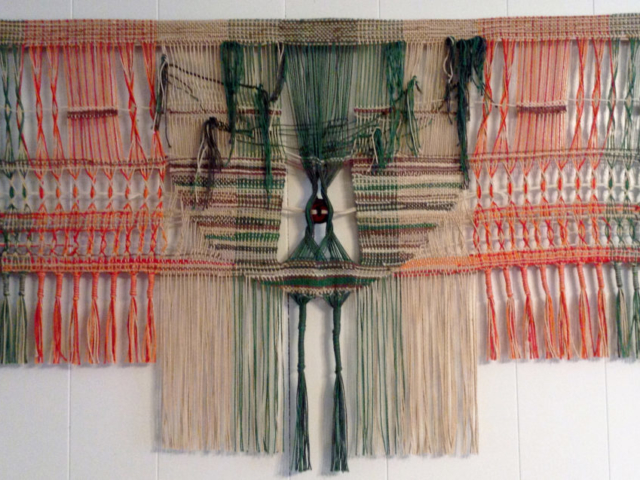 Woven wall hanging by fiber artist Petra Guenthner Johnson. Artwork depicts central tree-like form in greens and brown. There is leno work on either side in red and orange. Diemensions: 35x21"