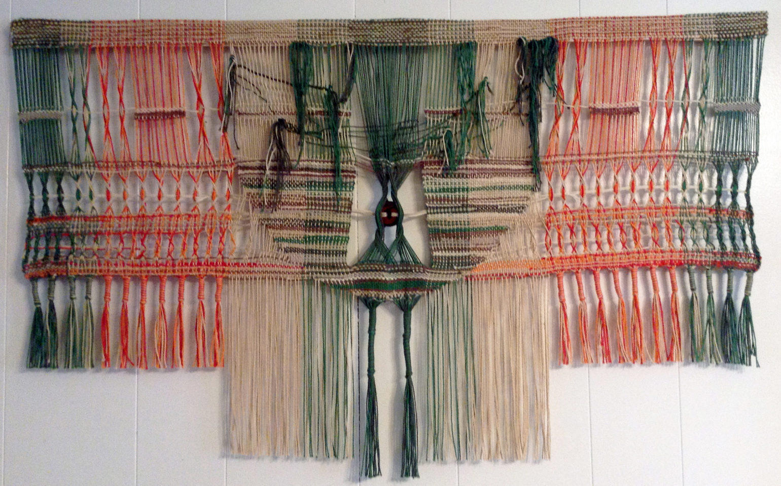 Woven wall hanging by fiber artist Petra Guenthner Johnson. Artwork depicts central tree-like form in greens and brown. There is leno work on either side in red and orange. Diemensions: 35x21"