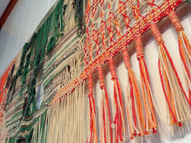 Woven wall hanging by fiber artist Petra Guenthner Johnson. Close-up of fringe and leno details in red, orange, and greens.