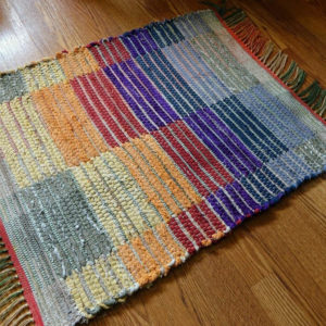 Rag rug woven by fiber artist Petra Guenthner Johnson. Rug with blocks of color alternating in rainbow order. Made with repurposed materials and cotton rug warp. Approximate size 24x36".