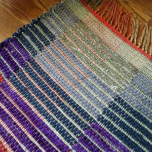 Detail of rag rug woven by fiber artist Petra Guenthner Johnson. Close up of rug with blocks of color alternating in rainbow order. Made with repurposed materials and cotton rug warp. Approximate size 24x36".