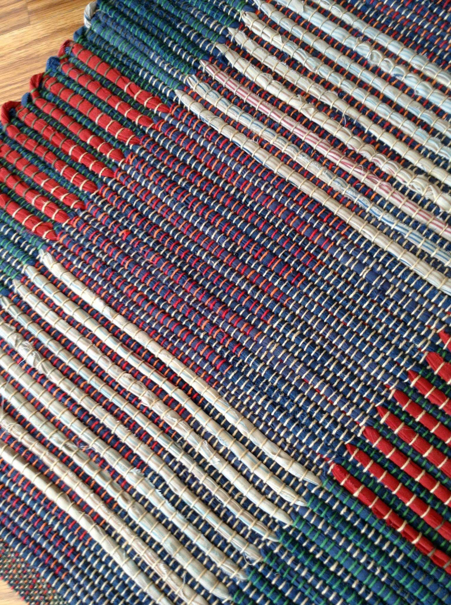 Detail of rag rug woven by fiber artist Petra Guenthner Johnson. Detail shows close-up of rug with navy background with alternating blocks or red and off-white. Made with repurposed materials and cotton rug warp. Approximate size 34x20".