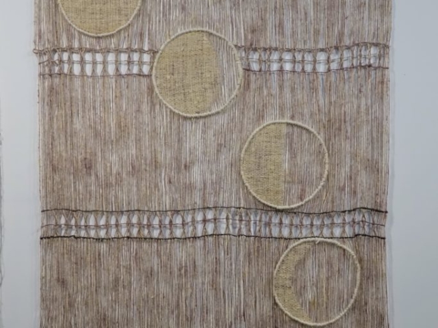 Woven artwork by fiber artist Petra Guenthner Johnson. Image of open woven pink and gray panel with waning moon phases, woven in off-white, moving in an arc from left to right across the panel. 32x45"