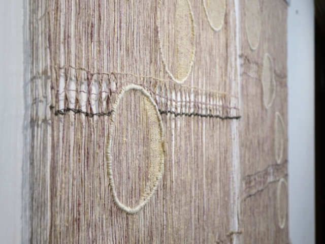 Detail of woven artwork by fiber artist Petra Guenthner Johnson. Image of two open woven pink and gray panels with images of moon phases, woven in off-white, moving in a half circle across them. Each panel is 32x45"