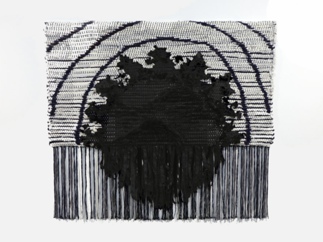 Woven rag wall hanging by fiber artist Petra Guenthner Johnson. Artwork has white background with black circular form in its center. Three half circles radiate away from center. 34x22"